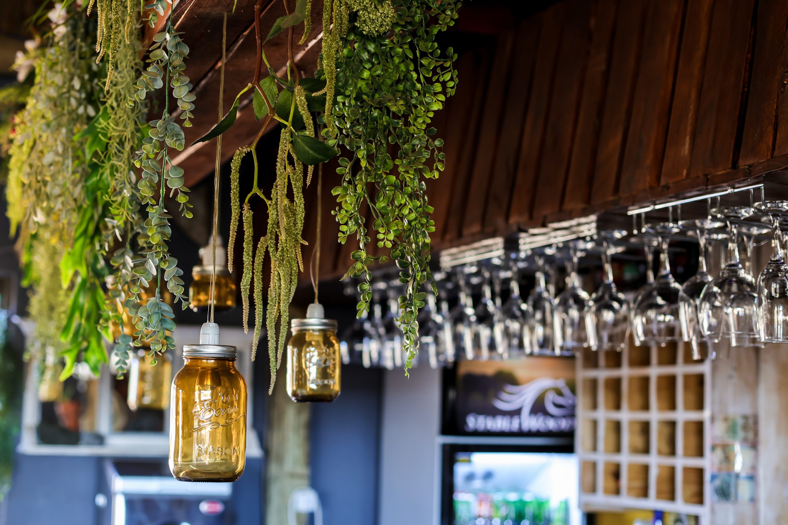 A warm and inviting bar area at Stablewood Lodge, featuring hanging plants, unique mason jar lights, and a display of wine glasses, creating a rustic and cosy atmosphere.